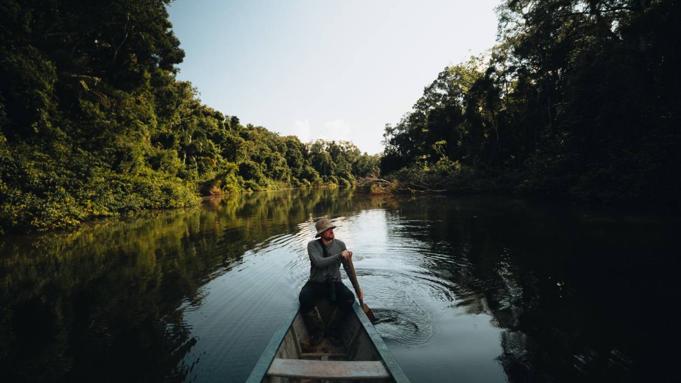A guide paddling a canoe down a still, forest-lined river