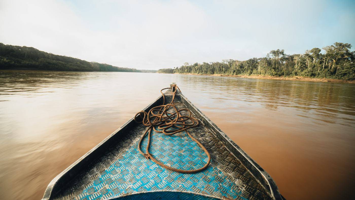The bow of a river boat heading down the wide brown Madre de Dios River