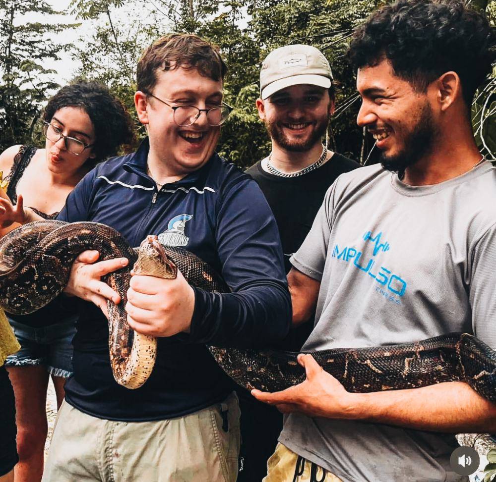 A local guide and travelers holding a boa together in the forest
