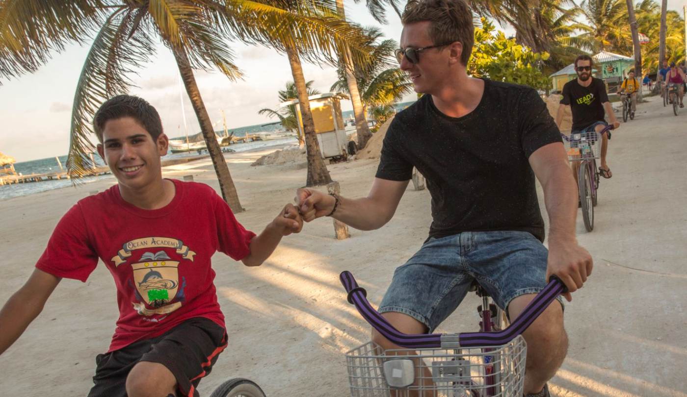 A Belizean student and a visiting student bumping fists while biking along the Caye Caulker waterfront
