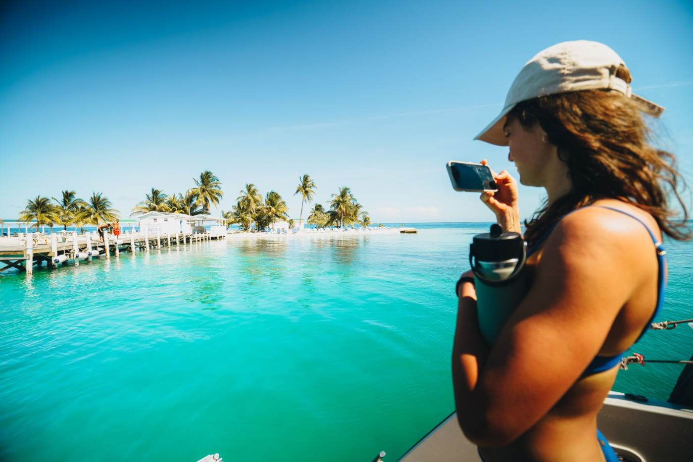 A student photographing a palm-lined caye and dock from the bow of a boat