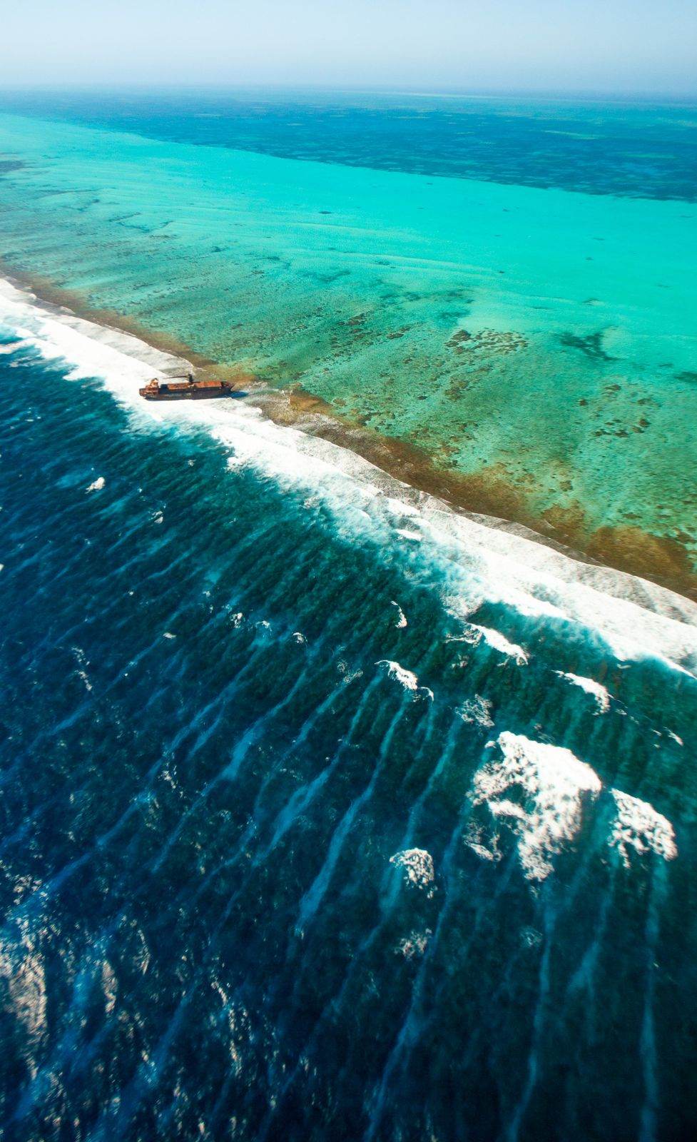 Aerial view of the Belize Barrier Reef, with a shipwreck on the reef crest between deep water and the turquoise lagoon
