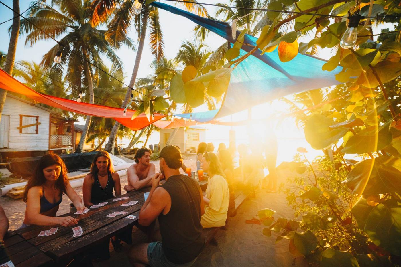 The group playing cards at a long table under shade sails at sunset