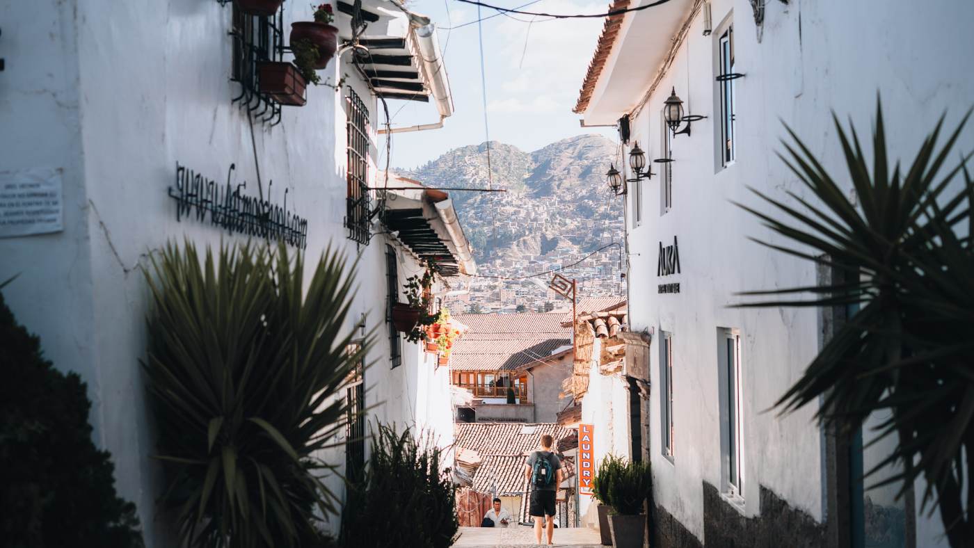 A narrow whitewashed street in Cusco's San Blas quarter with hills beyond