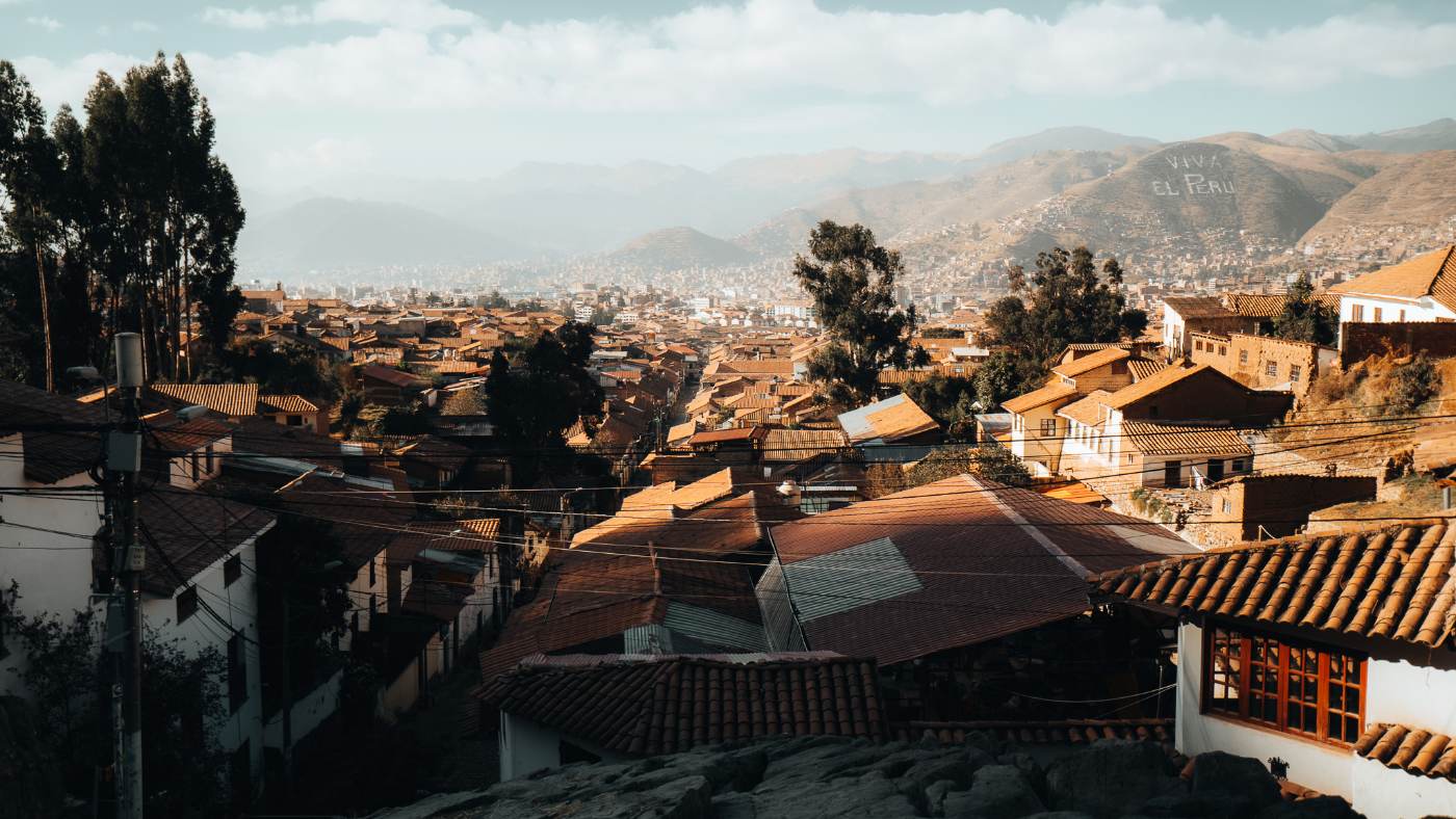 Late sun over Cusco's tiled rooftops, with hills and the Viva el Peru hillside lettering beyond