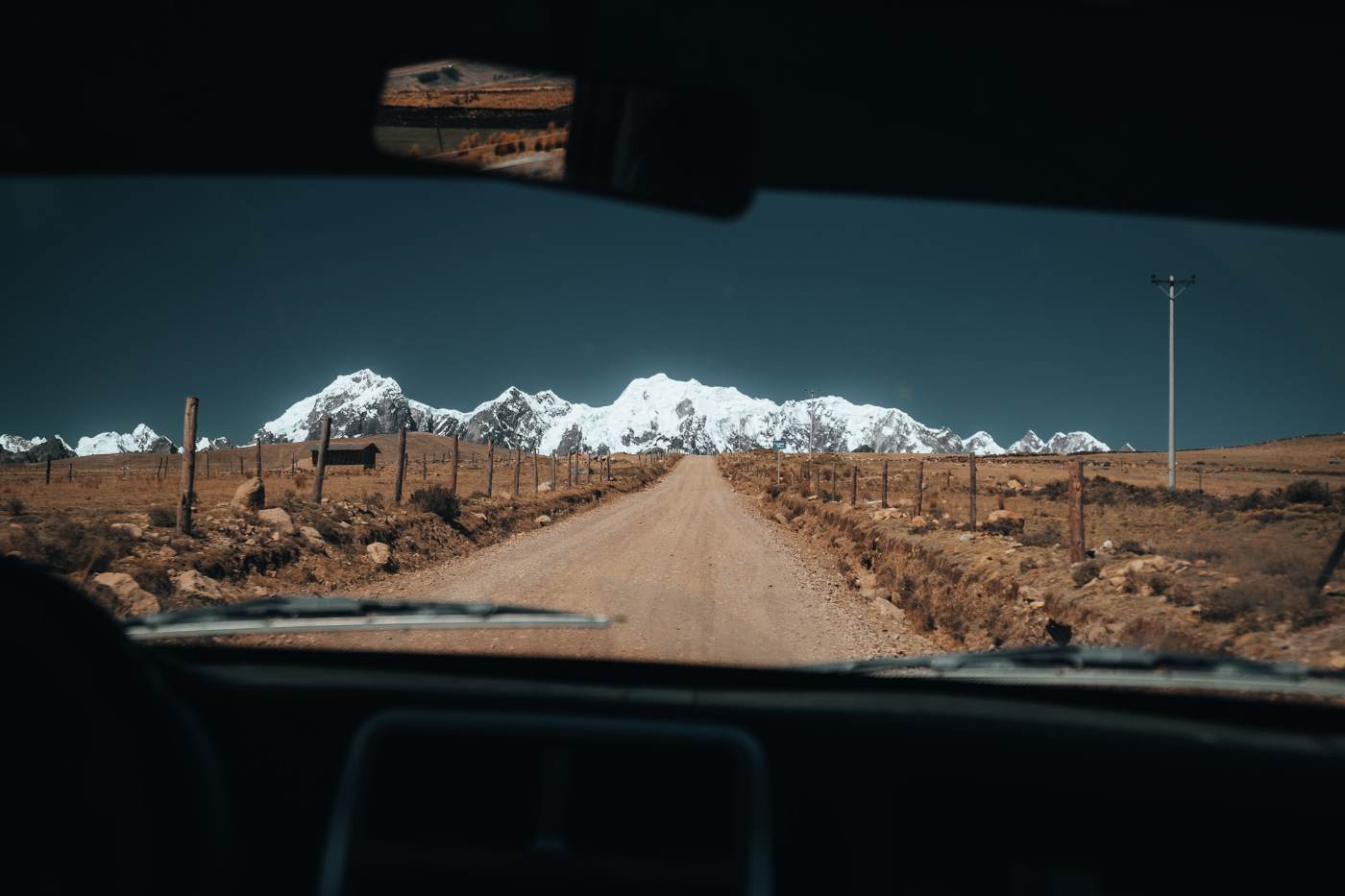 A dirt road across the high puna toward a glaciated range, seen through a windshield