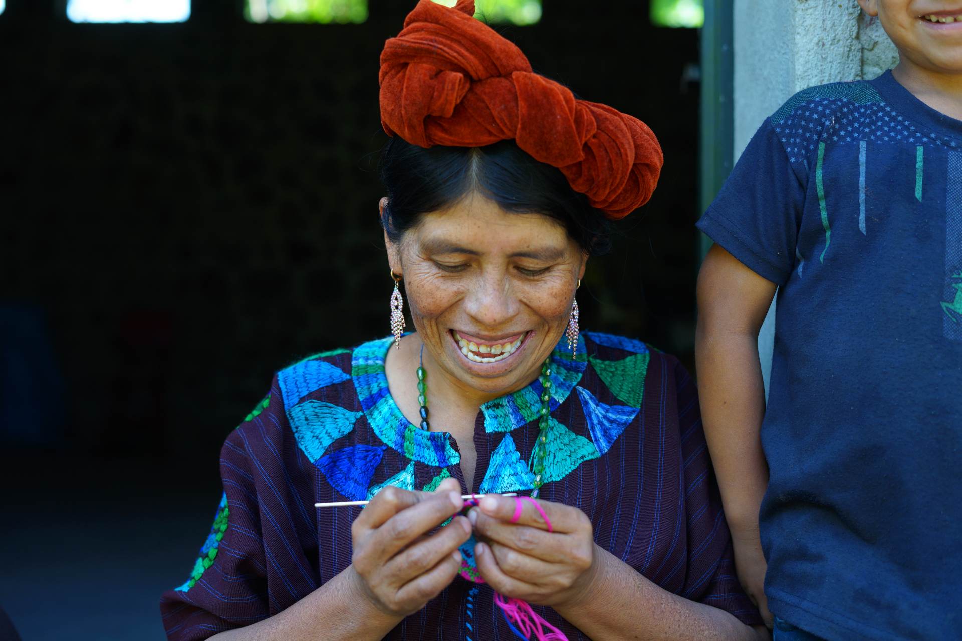 A Maya artisan smiling as she crochets in an embroidered huipil