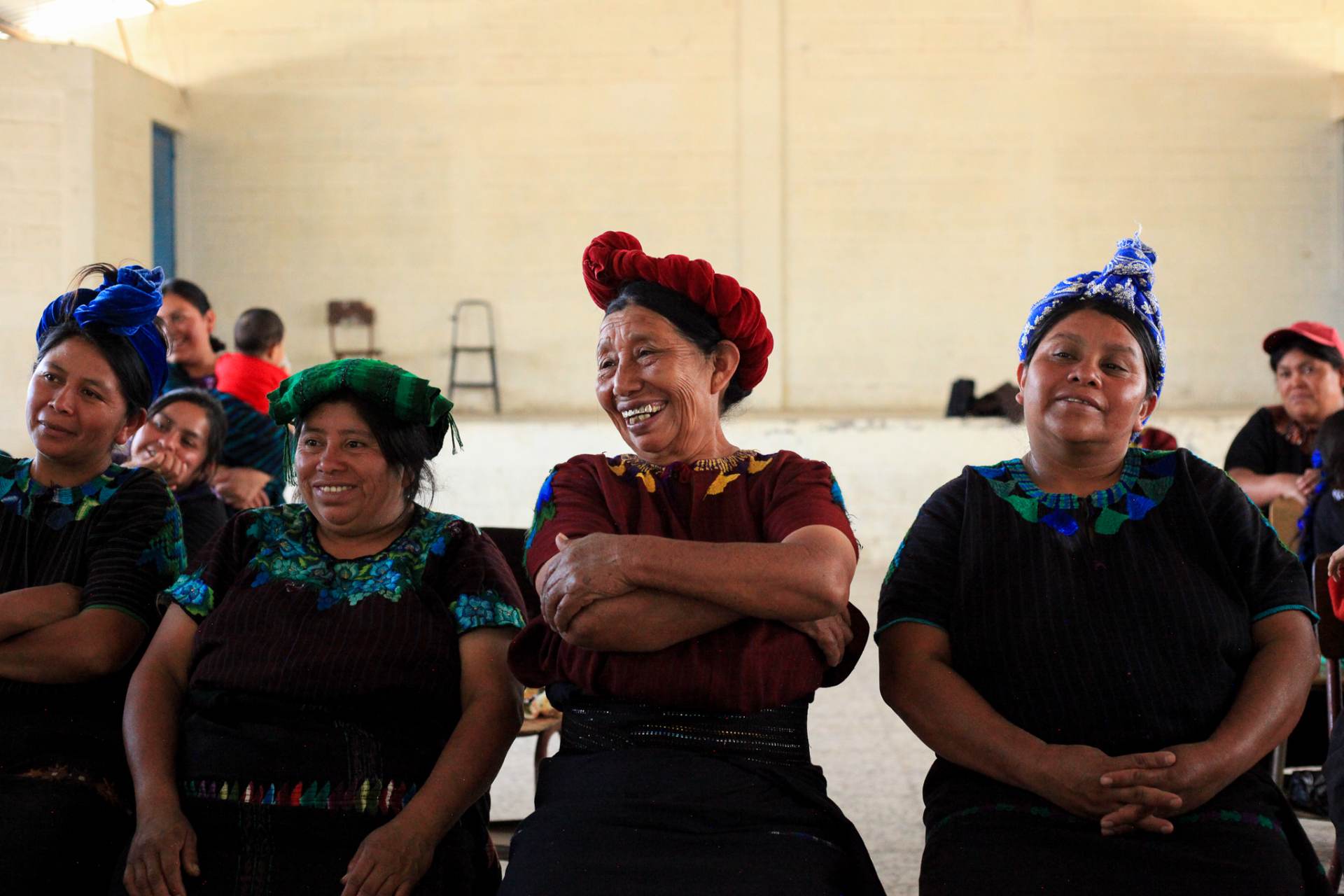 Tz'utujil women in traditional headwraps laughing together during a community meeting
